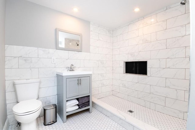 bathroom featuring toilet, recessed lighting, vanity, tile walls, and a tile shower