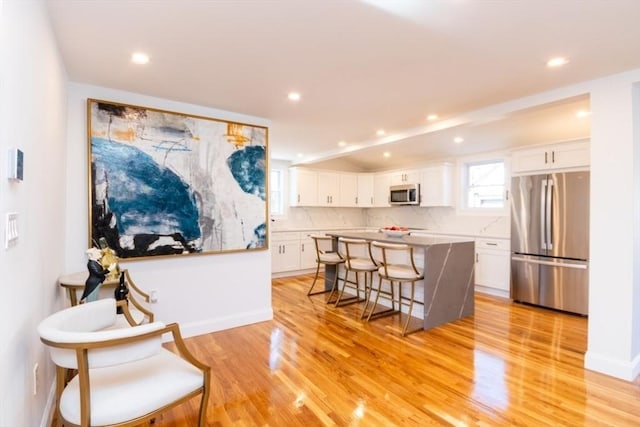 kitchen with white cabinets, decorative backsplash, appliances with stainless steel finishes, a kitchen breakfast bar, and light wood-type flooring