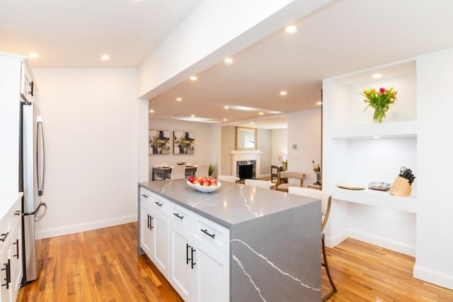 kitchen with freestanding refrigerator, a center island, white cabinetry, and light wood finished floors