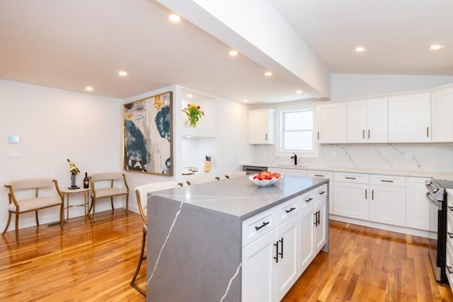 kitchen featuring light wood-style flooring, white cabinets, backsplash, a center island, and stainless steel electric range oven