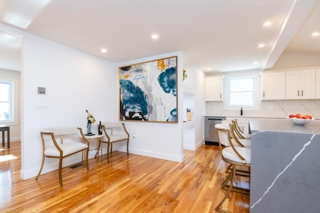 kitchen featuring backsplash, stainless steel dishwasher, light wood-style floors, white cabinetry, and baseboards