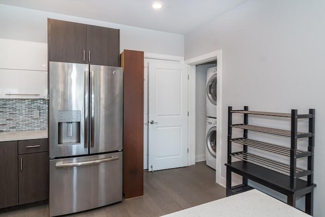 kitchen with stainless steel fridge, dark wood-type flooring, tasteful backsplash, stacked washing maching and dryer, and dark brown cabinetry