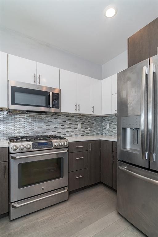 kitchen featuring white cabinets, backsplash, light hardwood / wood-style flooring, and appliances with stainless steel finishes