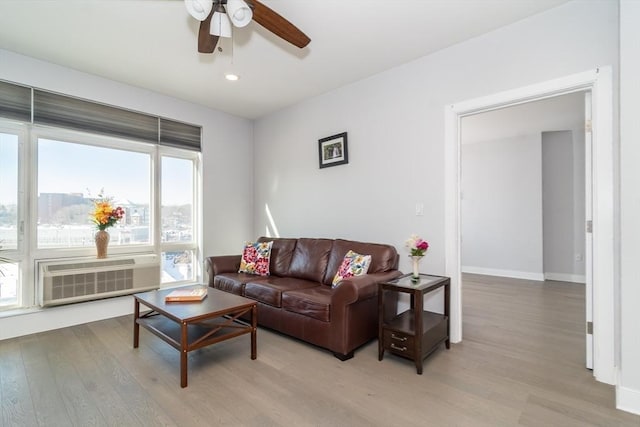 living room featuring ceiling fan, a wall mounted AC, and light hardwood / wood-style flooring