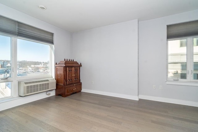 unfurnished room featuring an AC wall unit, plenty of natural light, and hardwood / wood-style flooring