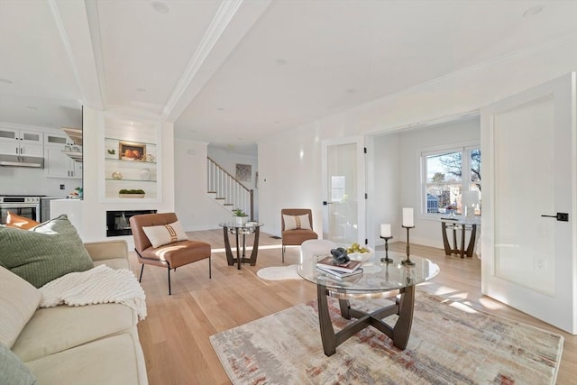 living room with light wood finished floors, baseboards, a glass covered fireplace, ornamental molding, and stairs