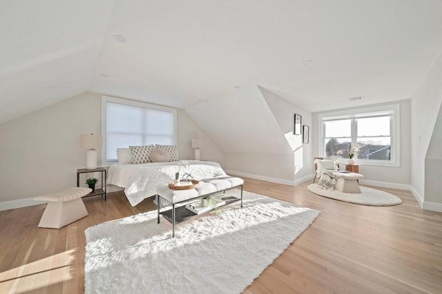 bedroom with vaulted ceiling, wood finished floors, visible vents, and baseboards