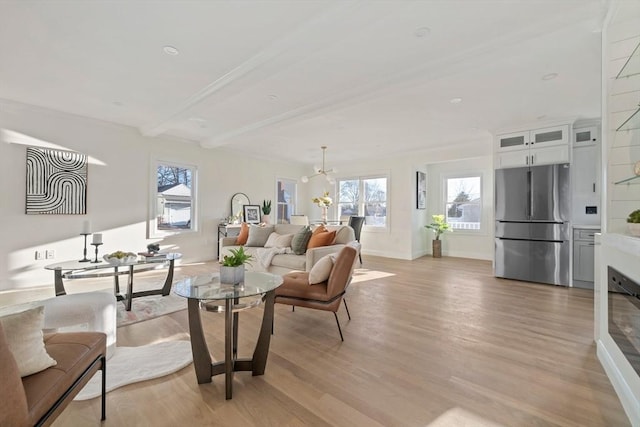 living area featuring baseboards, light wood finished floors, beam ceiling, and a notable chandelier