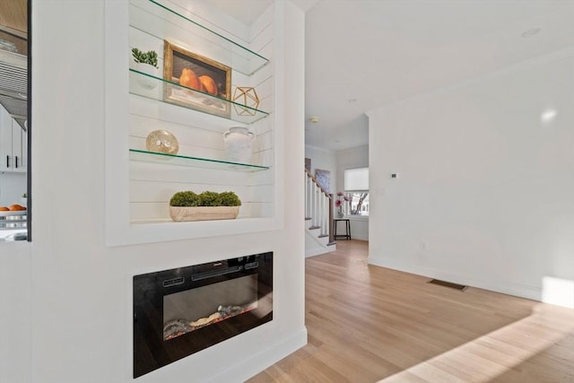 living area featuring visible vents, a glass covered fireplace, stairway, ornamental molding, and wood finished floors