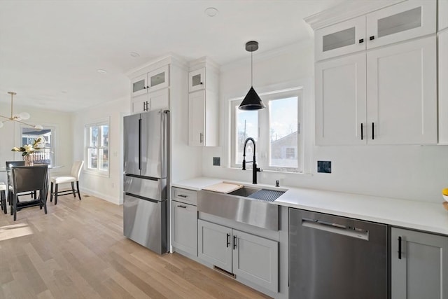 kitchen featuring pendant lighting, light countertops, appliances with stainless steel finishes, light wood-style floors, and a sink