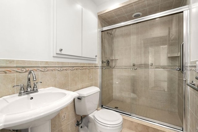 full bathroom featuring a sink, toilet, a stall shower, wainscoting, and tile walls