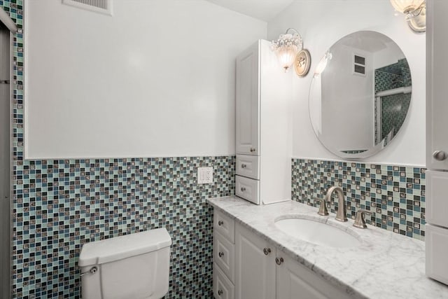 bathroom featuring toilet, vanity, tile walls, wainscoting, and tasteful backsplash