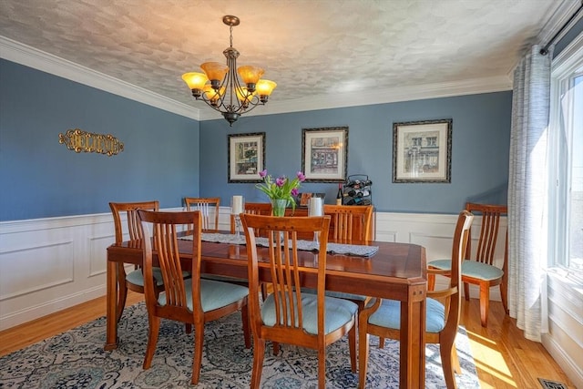 dining space featuring light wood-style floors, a wainscoted wall, a textured ceiling, and a notable chandelier
