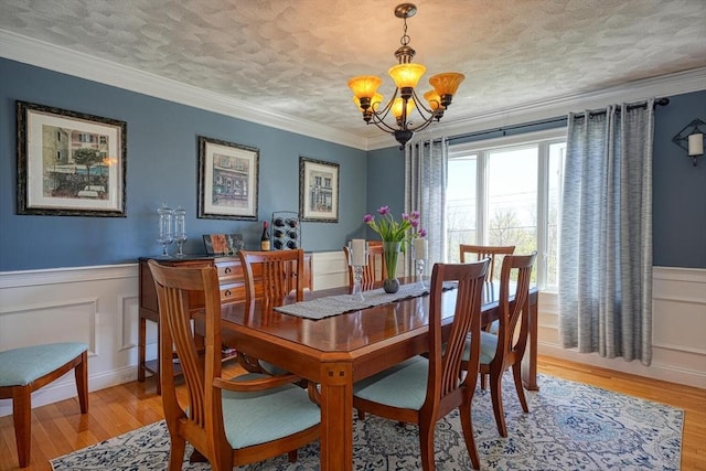 dining area with an inviting chandelier, light wood-style floors, a decorative wall, and wainscoting