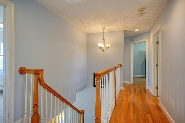 corridor featuring a notable chandelier, a textured ceiling, baseboards, an upstairs landing, and light wood-type flooring