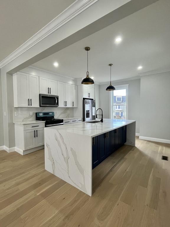 kitchen with appliances with stainless steel finishes, a large island with sink, light hardwood / wood-style flooring, white cabinetry, and hanging light fixtures