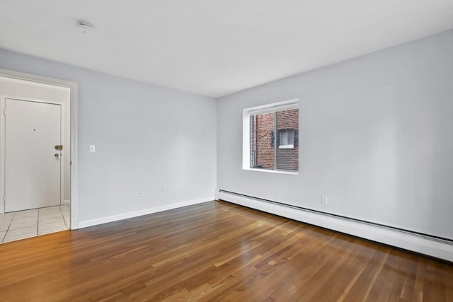 spare room featuring a baseboard radiator, baseboards, and wood finished floors