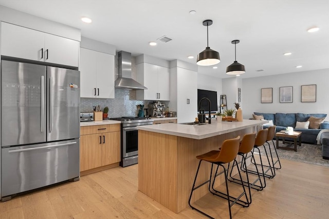 kitchen with appliances with stainless steel finishes, sink, wall chimney range hood, white cabinets, and an island with sink