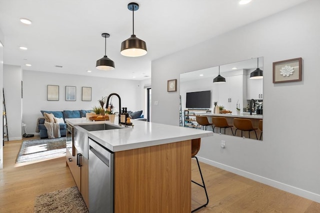 kitchen with a breakfast bar, hanging light fixtures, stainless steel dishwasher, light wood-type flooring, and an island with sink