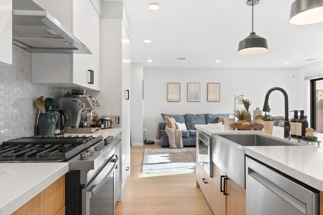 kitchen with light stone countertops, appliances with stainless steel finishes, wall chimney exhaust hood, white cabinetry, and hanging light fixtures