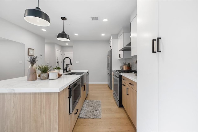 kitchen featuring hanging light fixtures, an island with sink, light brown cabinetry, white cabinetry, and stainless steel appliances