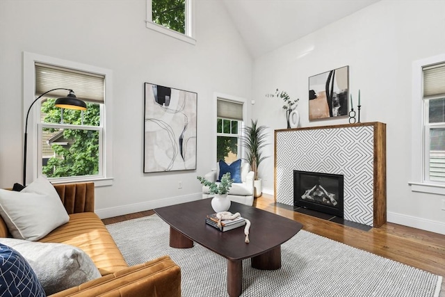 living area with plenty of natural light, wood finished floors, a tile fireplace, baseboards, and high vaulted ceiling