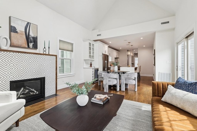 living area featuring plenty of natural light, dark wood-style floors, a tiled fireplace, and high vaulted ceiling