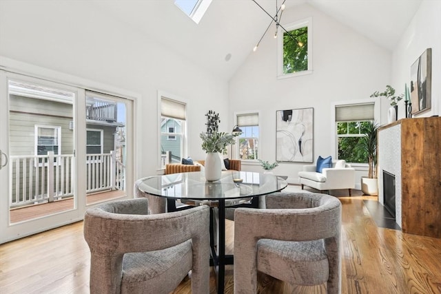 dining space with wood finished floors, healthy amount of natural light, high vaulted ceiling, and a fireplace with flush hearth