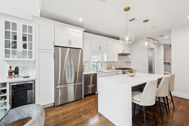 kitchen with stainless steel appliances, beverage cooler, a kitchen island, light countertops, and a breakfast bar