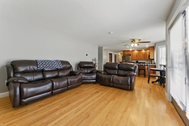 living room featuring ceiling fan, baseboards, a healthy amount of sunlight, and light wood-style flooring
