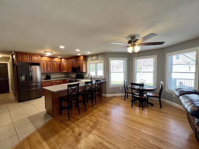 kitchen featuring a peninsula, baseboards, gas range, black microwave, and refrigerator with ice dispenser