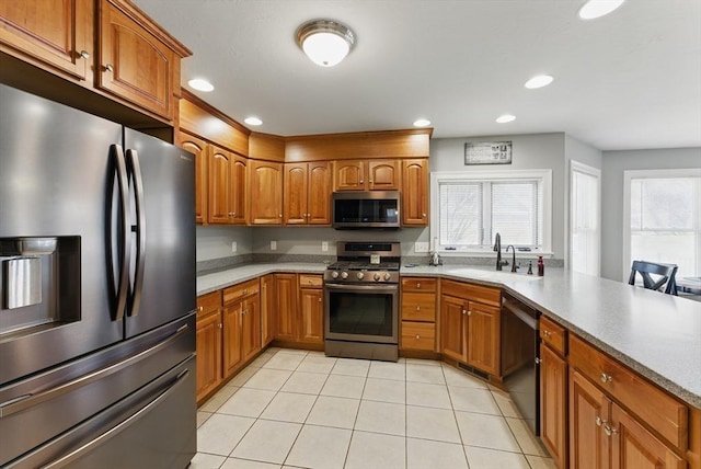 kitchen featuring brown cabinets, a sink, light tile patterned flooring, a peninsula, and appliances with stainless steel finishes