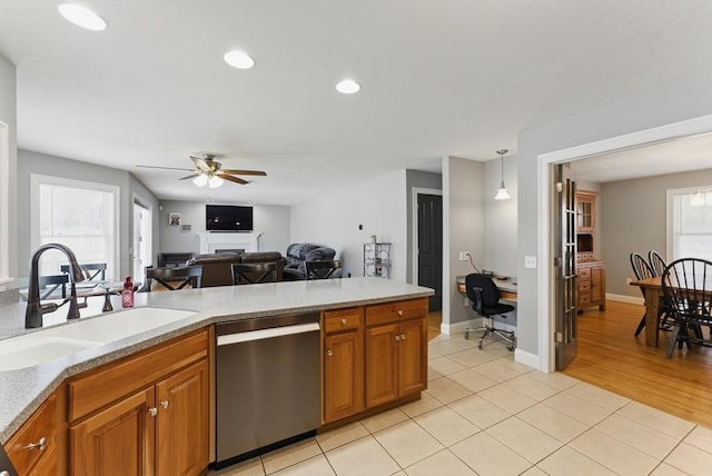 kitchen featuring stainless steel dishwasher, a sink, a ceiling fan, brown cabinetry, and light countertops