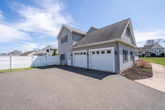view of property exterior featuring a gate, aphalt driveway, fence, a garage, and roof with shingles