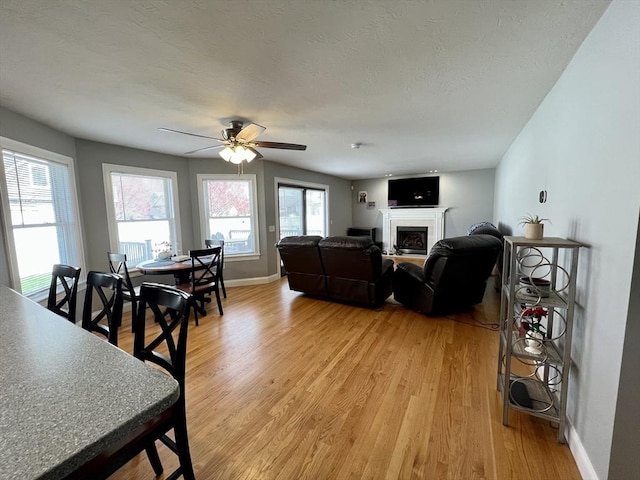 living area with light wood-type flooring, baseboards, a fireplace, and ceiling fan
