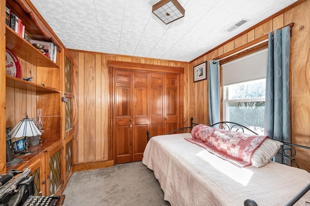 bedroom with visible vents, light colored carpet, a closet, and wooden walls