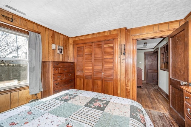 bedroom with wood finished floors, visible vents, ornamental molding, a closet, and wood walls