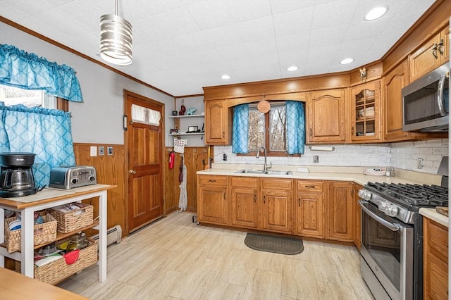 kitchen featuring brown cabinets, a sink, appliances with stainless steel finishes, wainscoting, and light countertops