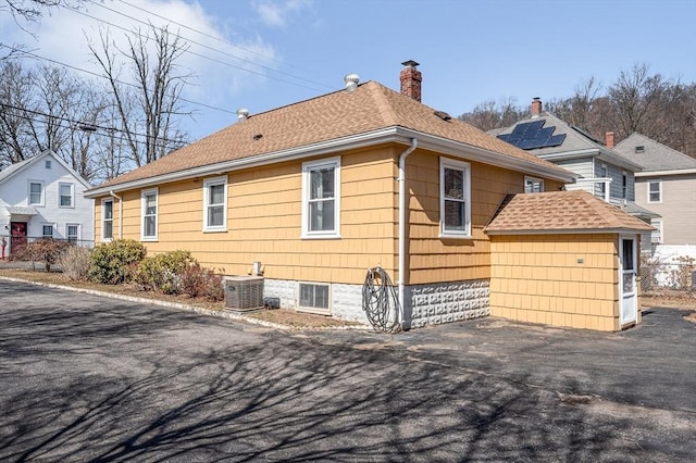 view of home's exterior featuring central AC, fence, a storage shed, an outdoor structure, and a chimney