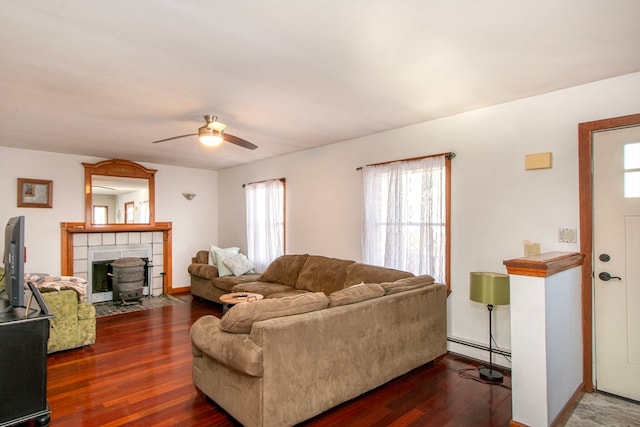 living room featuring a baseboard radiator, dark wood-type flooring, a wood stove, and ceiling fan