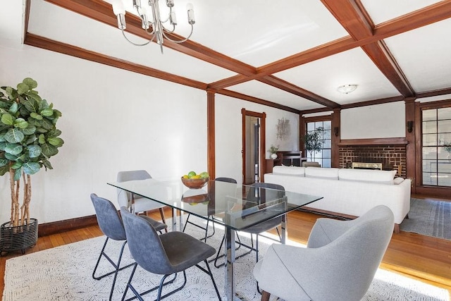 dining room with beamed ceiling, a fireplace, a notable chandelier, light hardwood / wood-style flooring, and coffered ceiling