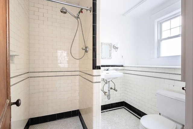 bathroom with tile patterned floors, toilet, tiled shower, and tile walls