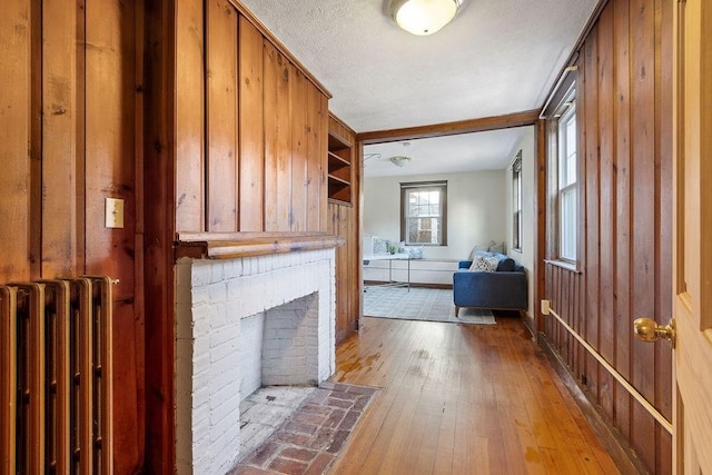 unfurnished living room with radiator, a textured ceiling, wood-type flooring, a brick fireplace, and wood walls