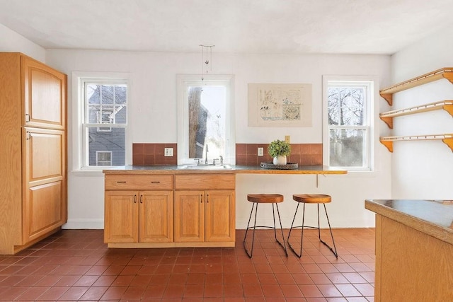 kitchen with a kitchen bar, sink, dark tile patterned flooring, and decorative light fixtures