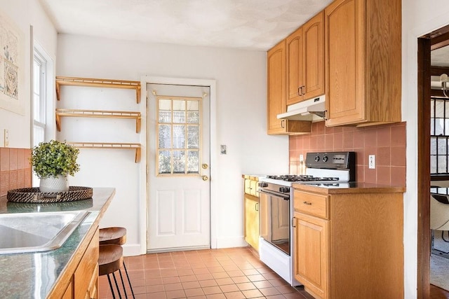 kitchen with white gas range, sink, backsplash, and light tile patterned floors