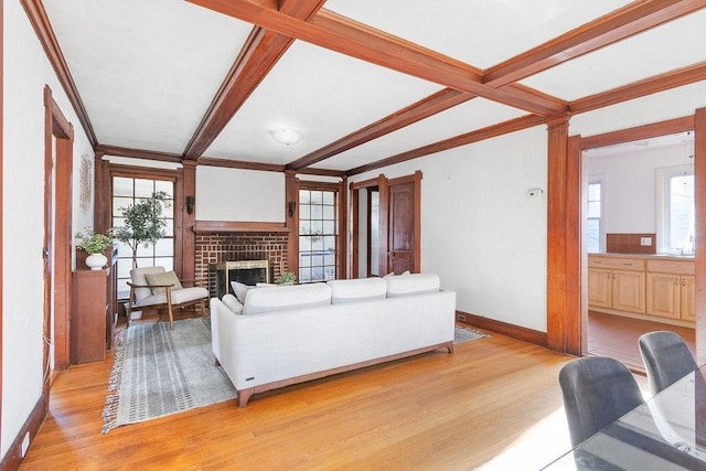 living room with a brick fireplace, ornamental molding, beamed ceiling, and light wood-type flooring