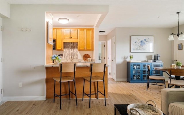 157 Franklin St Unit D3, Stoneham, MA 02180 - kitchen featuring light wood-style floors, a breakfast bar area, decorative backsplash, a peninsula, and pendant lighting