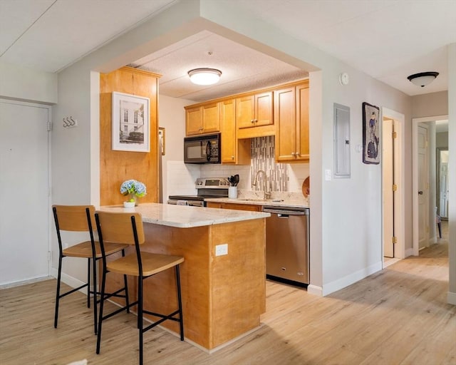 157 Franklin St Unit D3, Stoneham, MA 02180 - kitchen with appliances with stainless steel finishes, electric panel, a breakfast bar, backsplash, and light wood-style floors