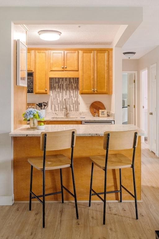 157 Franklin St Unit D3, Stoneham, MA 02180 - kitchen featuring light wood-style flooring, a breakfast bar, decorative backsplash, and light stone countertops