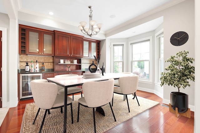 dining area with ornamental molding, wood-type flooring, wine cooler, and a chandelier